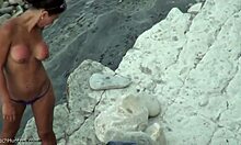Una tanga indossando il tanga mostra il suo culo su una spiaggia nudista